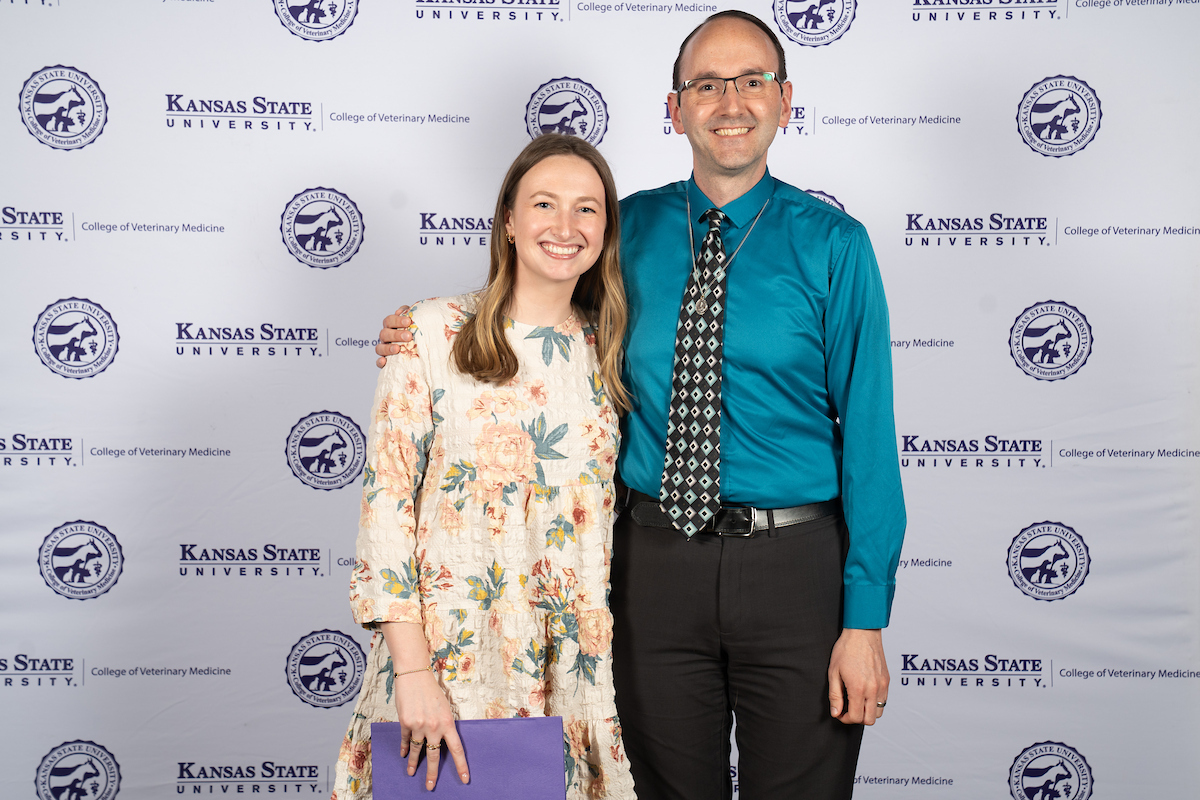 Two people stand in front of a backdrop smiling.