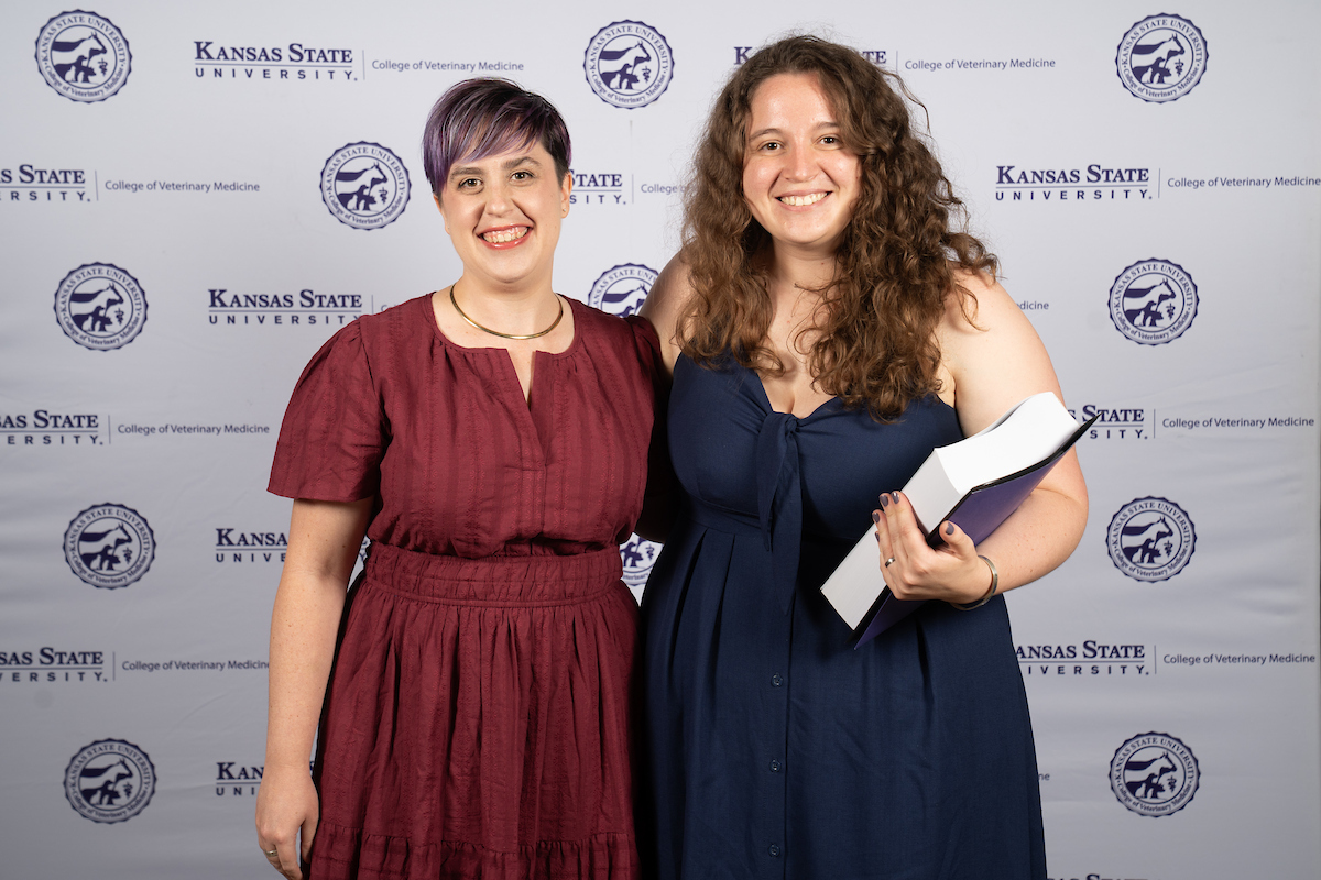 Two people stand in front of a backdrop smiling.