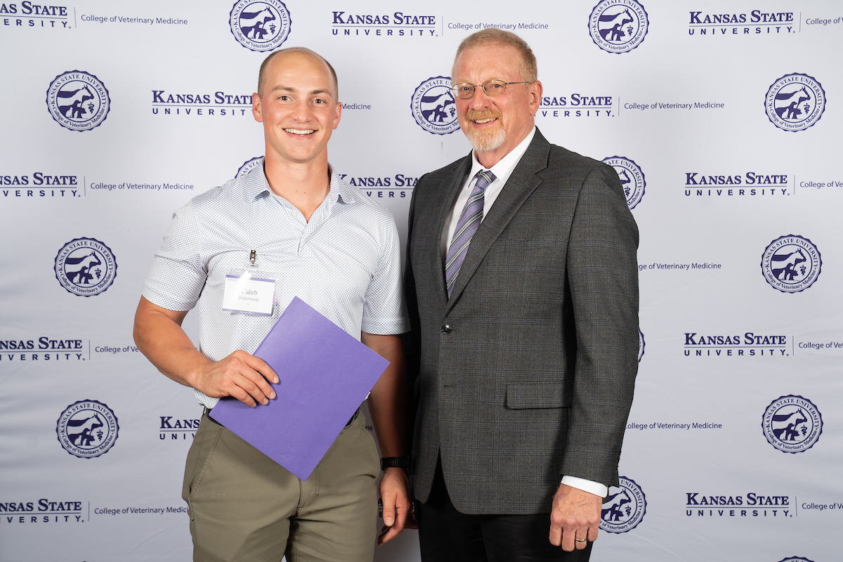 Two people stand in front of a backdrop smiling.