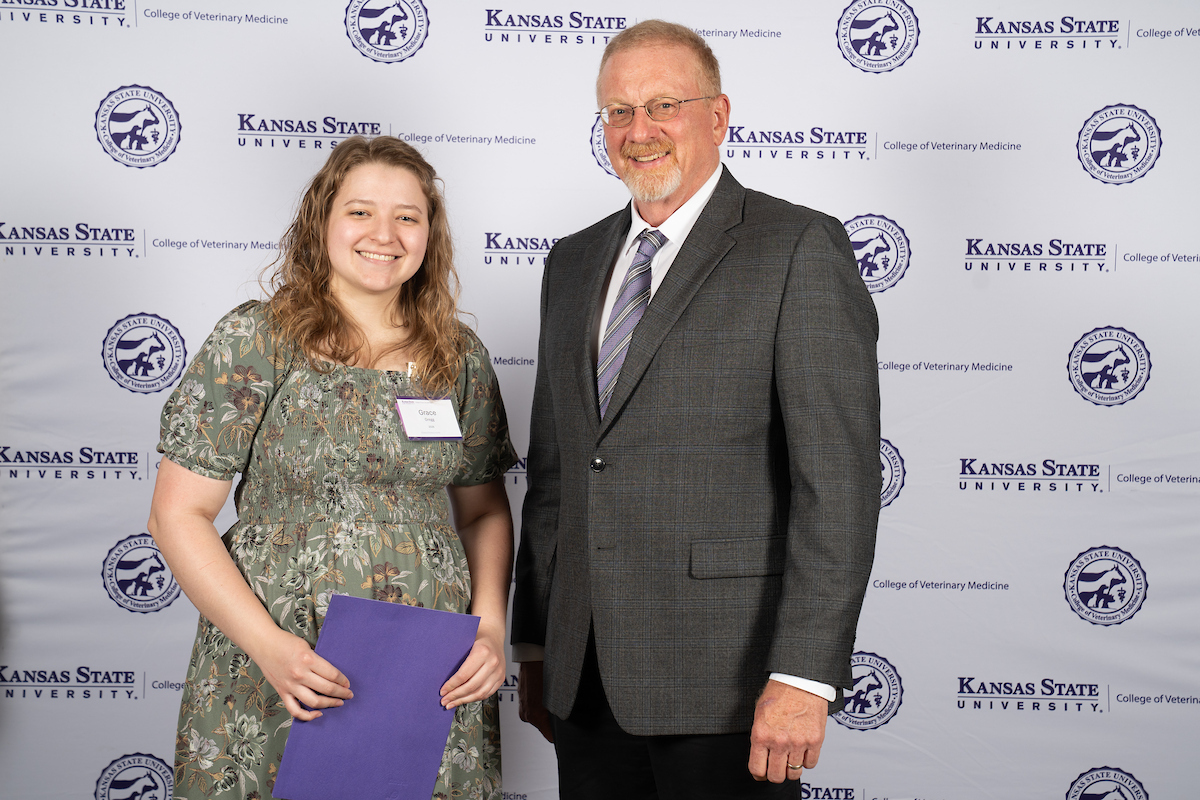 Two people stand in front of a backdrop smiling.