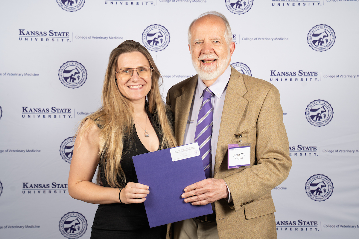 Two people stand in front of a backdrop smiling.