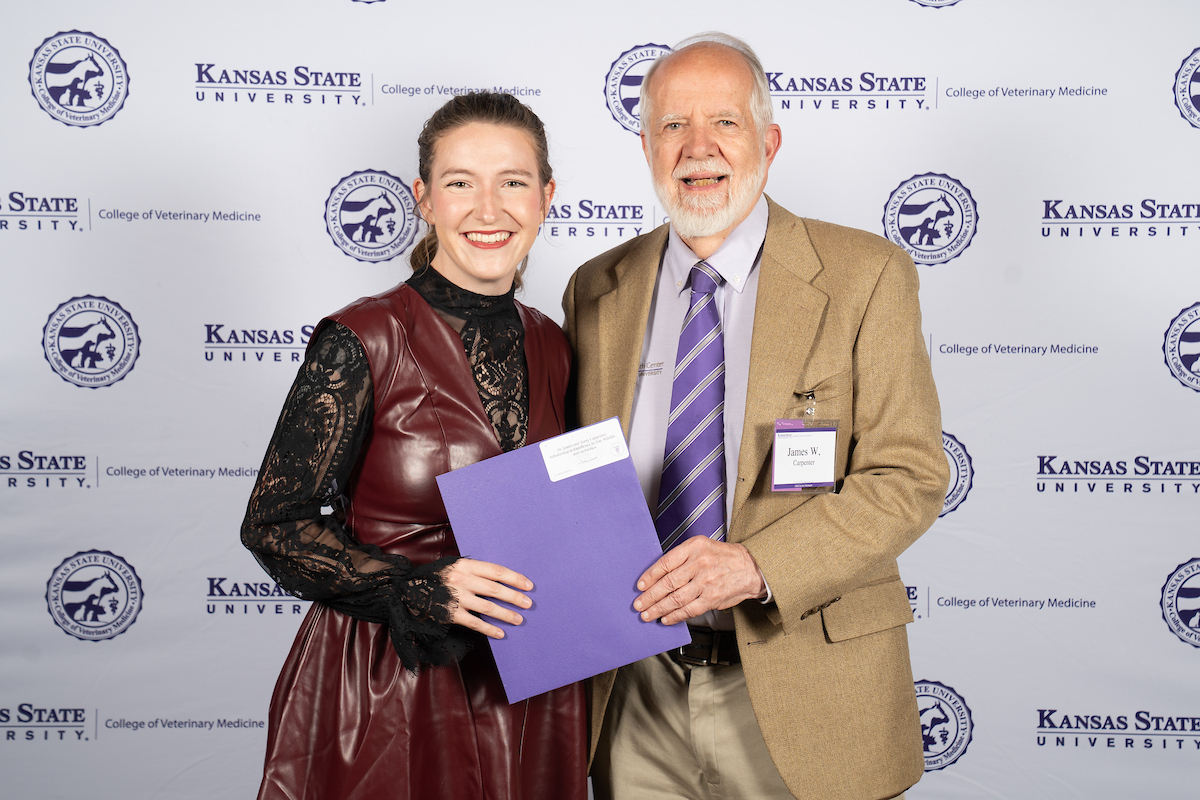 Two people stand in front of a backdrop smiling.