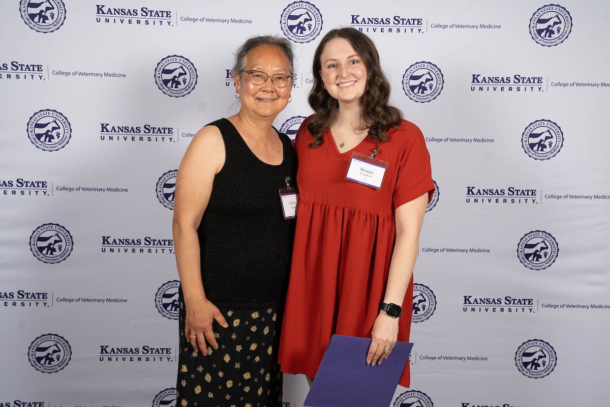 Two people stand in front of a backdrop smiling.