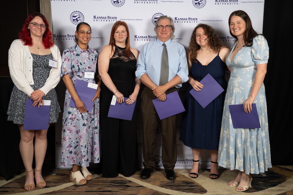 Six people stand in front of a backdrop smiling.