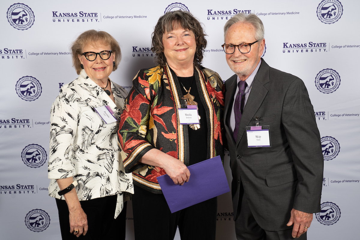 Three people stand in front of a backdrop smiling.