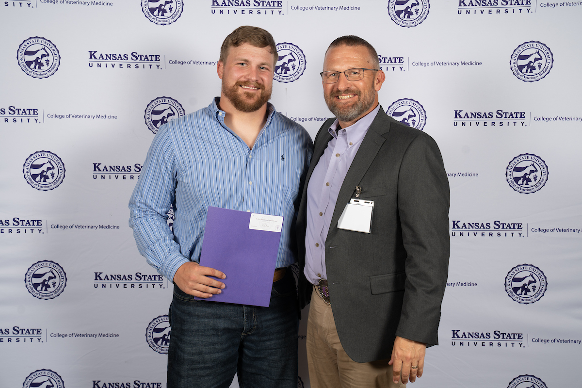 Two people stand in front of a backdrop smiling.