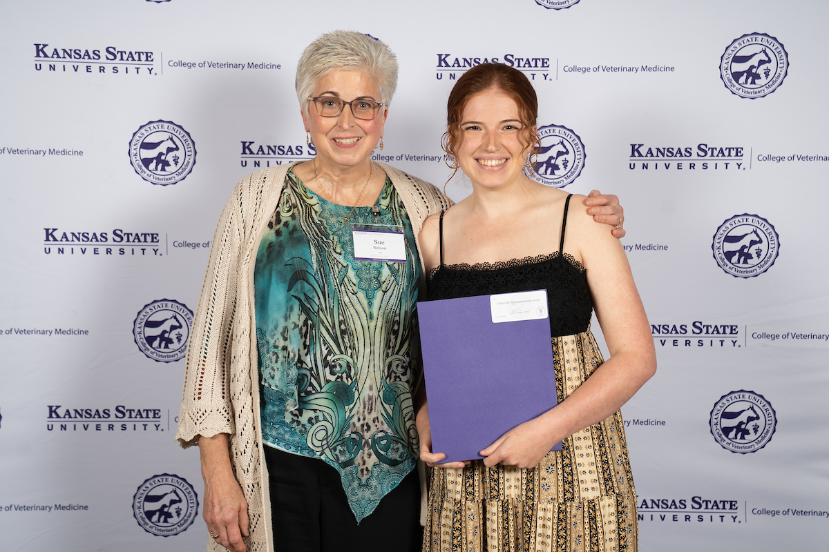 Two people stand in front of a backdrop smiling.