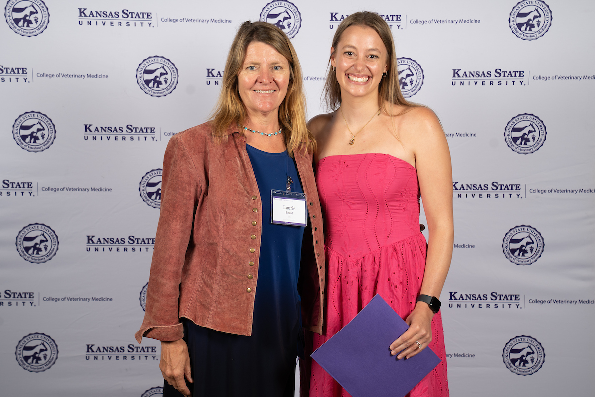 Two people stand in front of a backdrop smiling.