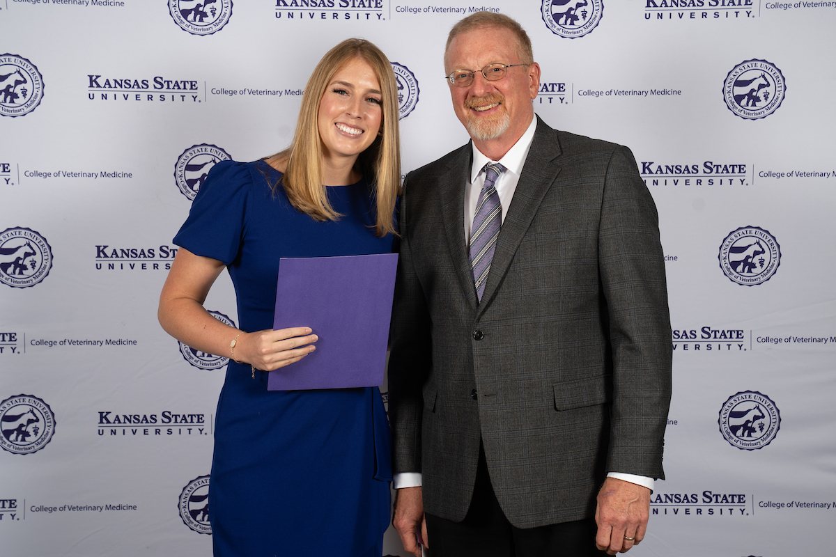 Two people stand in front of a backdrop smiling.
