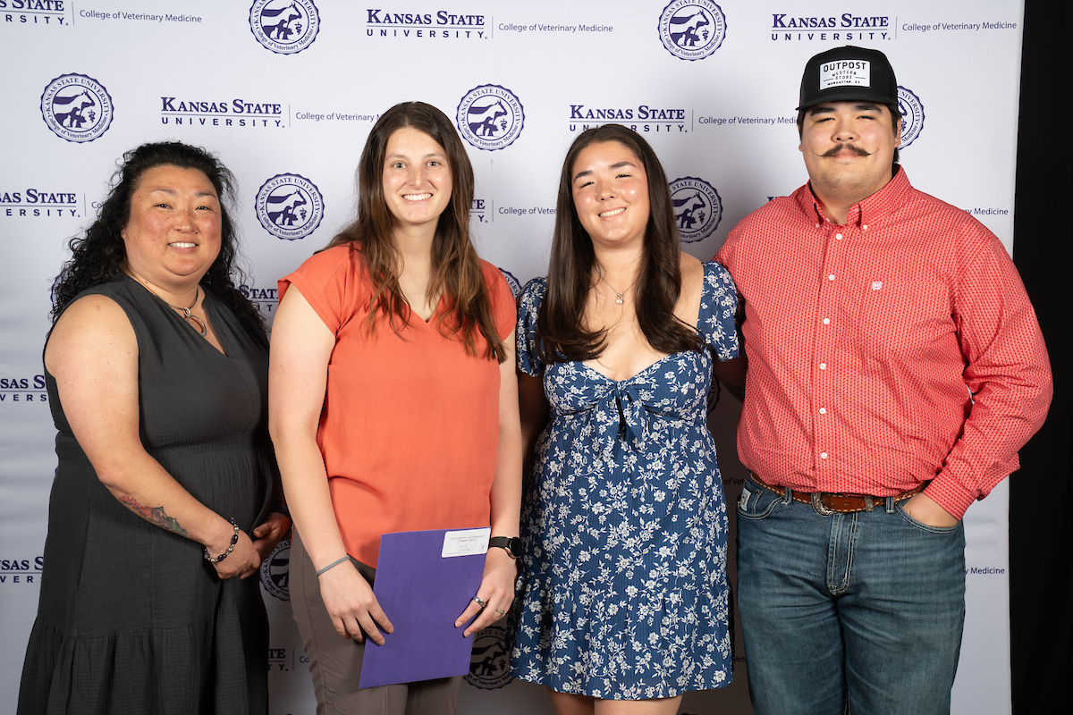 Four people stand in front of a backdrop smiling.