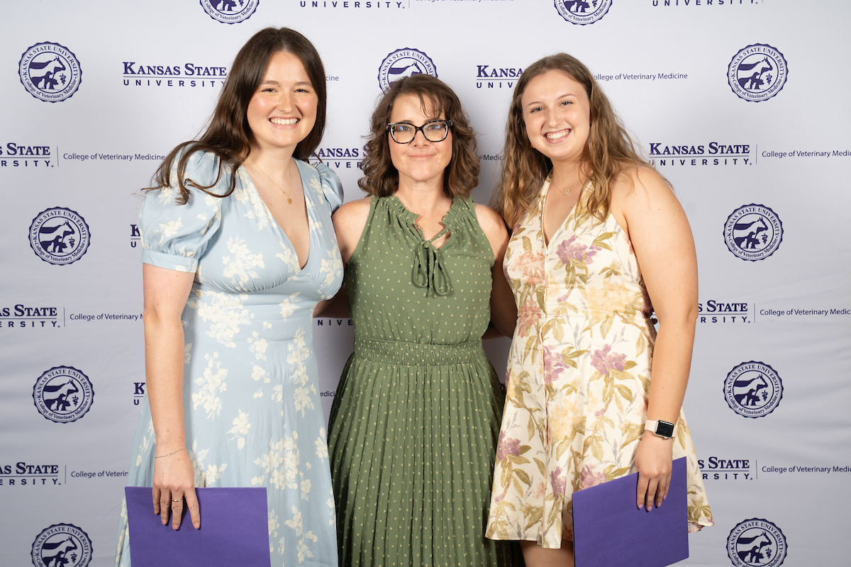 Three people stand in front of a backdrop smiling.