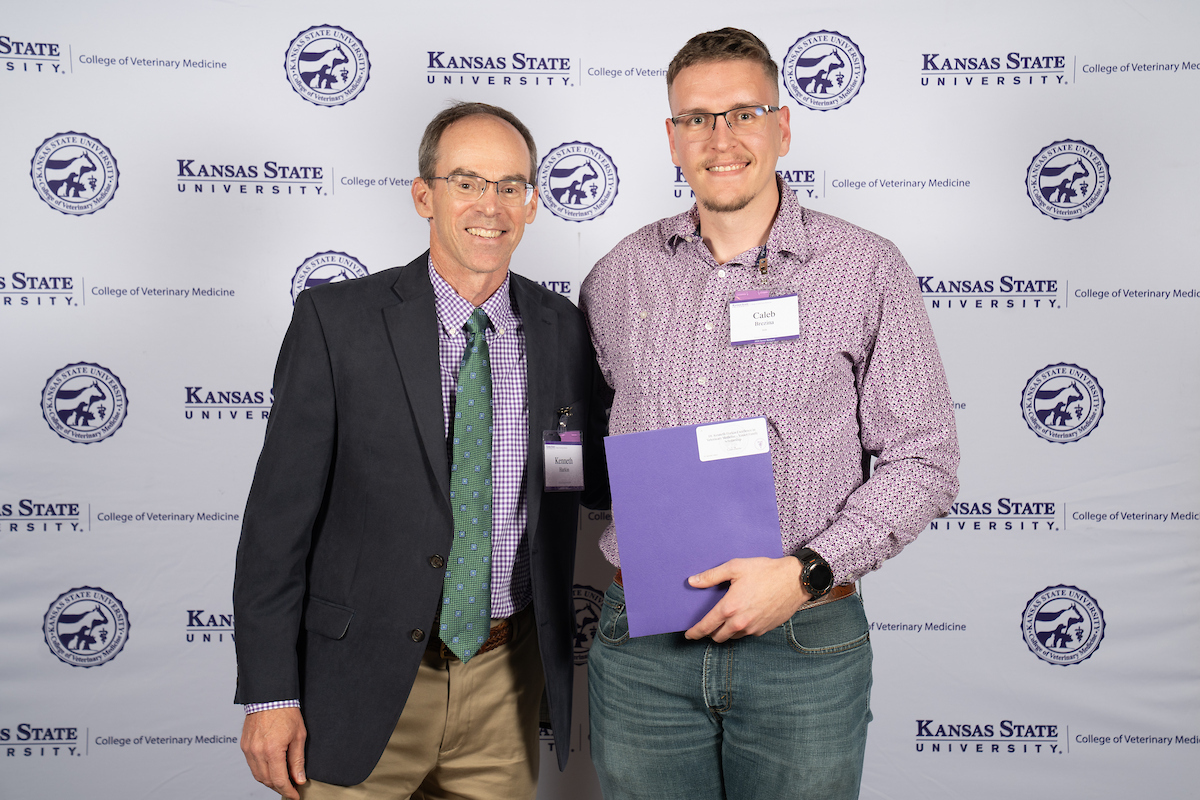 Two people stand in front of a backdrop smiling.