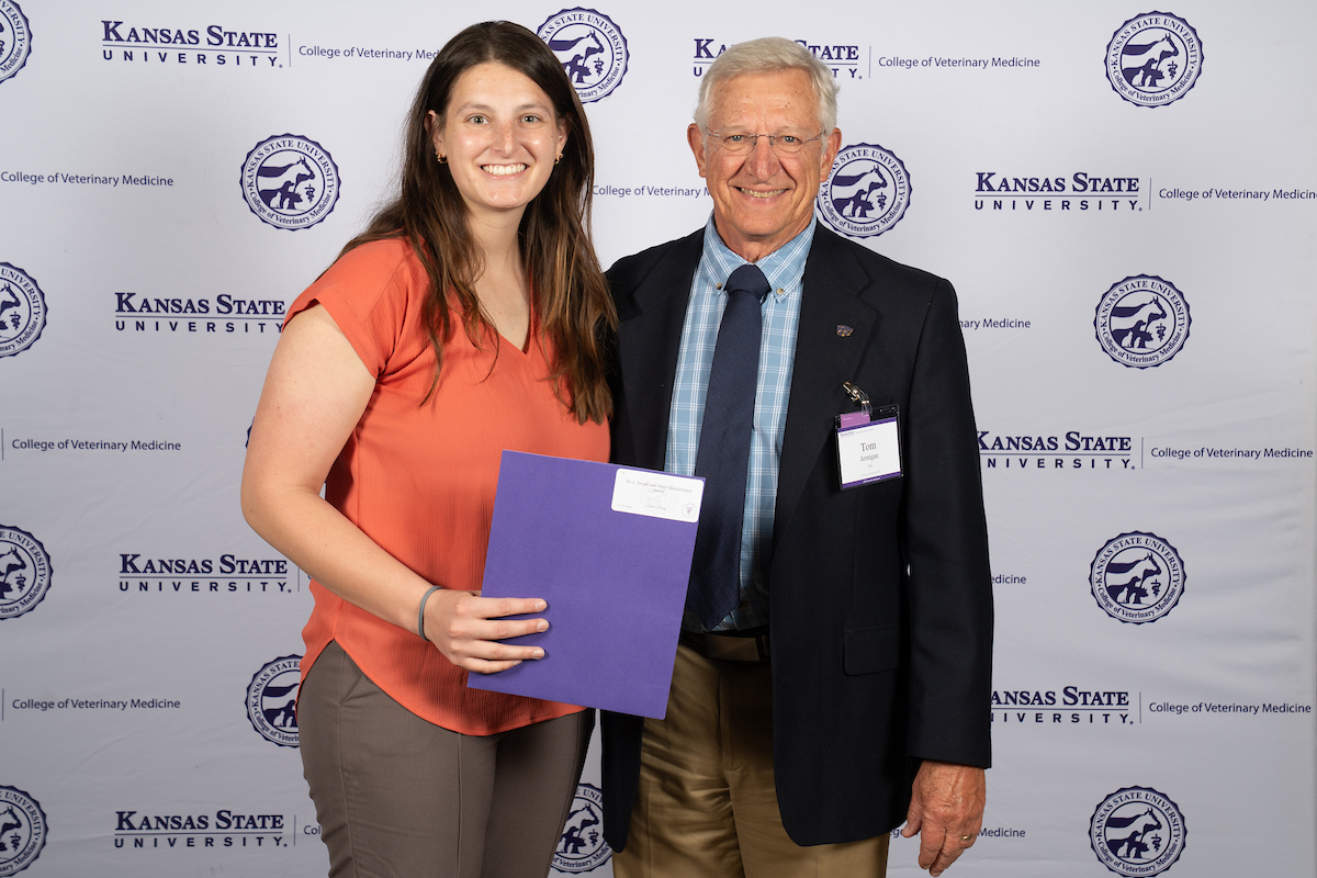 Two people stand in front of a backdrop smiling.