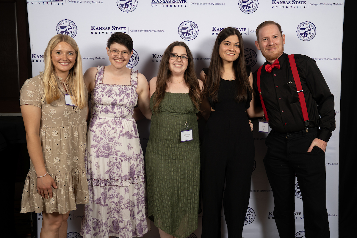 Four people stand in front of a backdrop smiling.