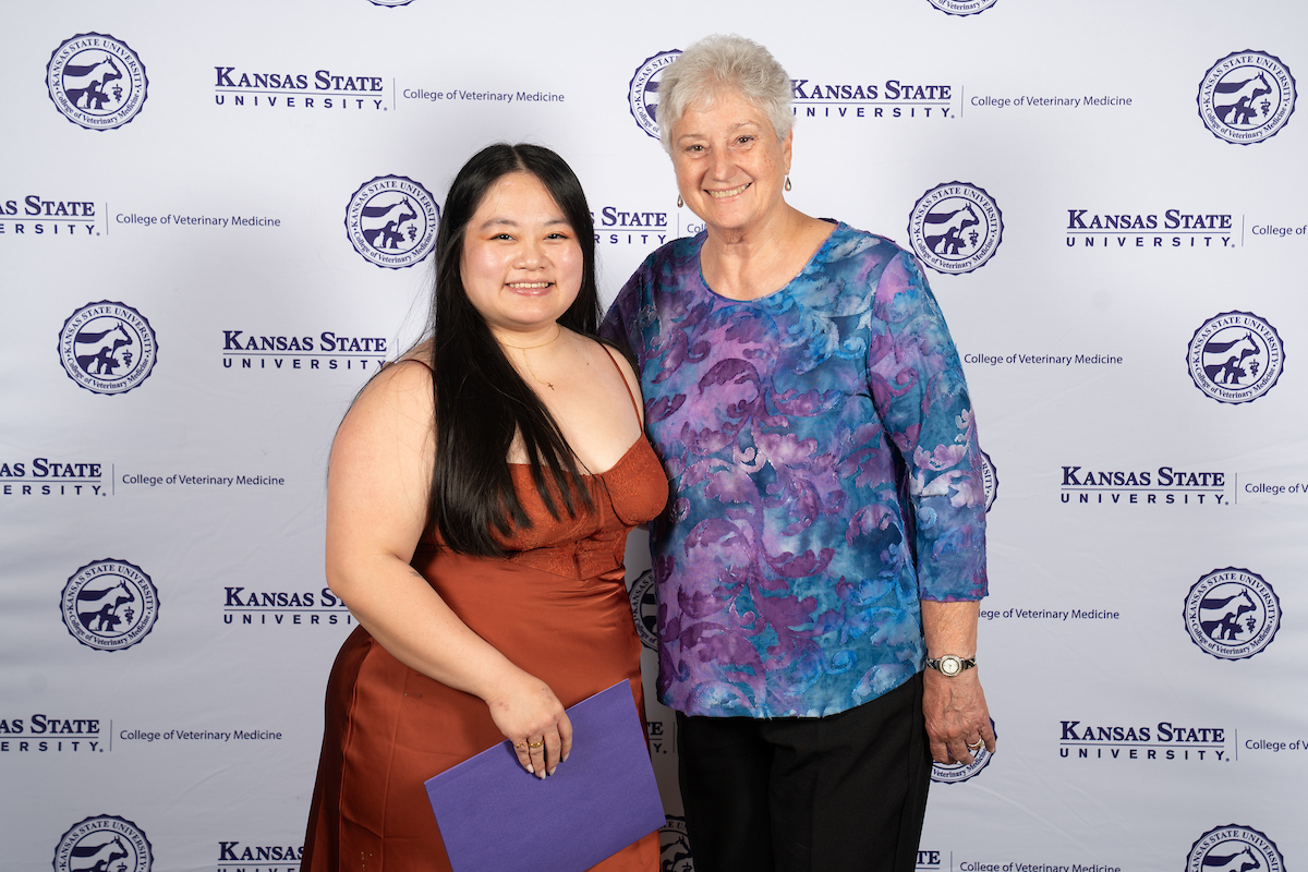 Two people stand in front of a backdrop smiling.