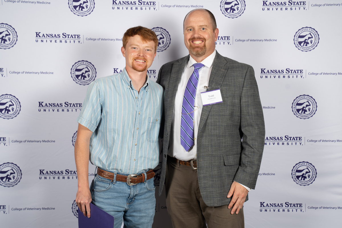Two people stand in front of a backdrop smiling.