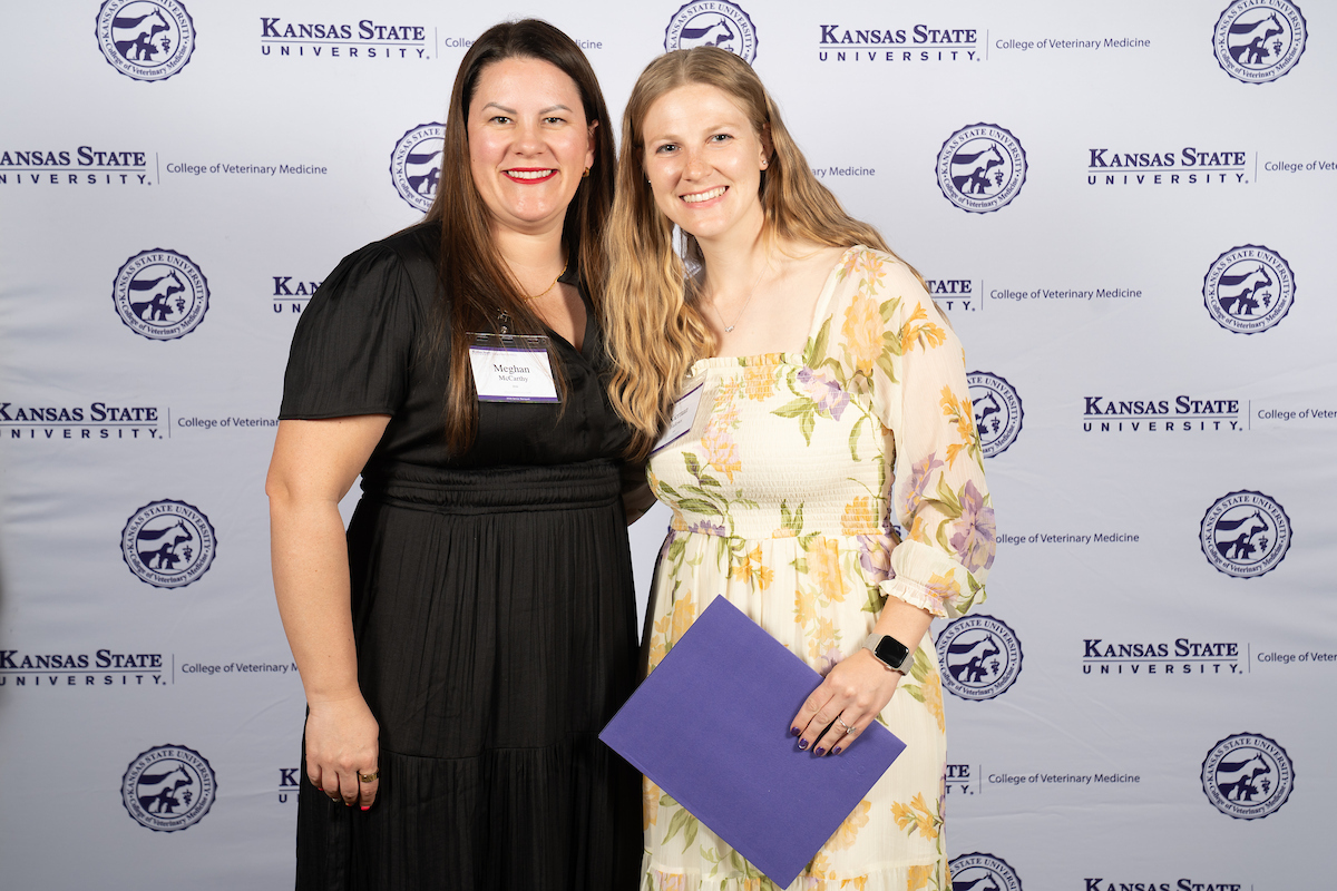 Two people stand in front of a backdrop smiling.