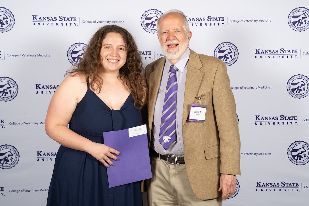 Two people stand in front of a backdrop smiling.