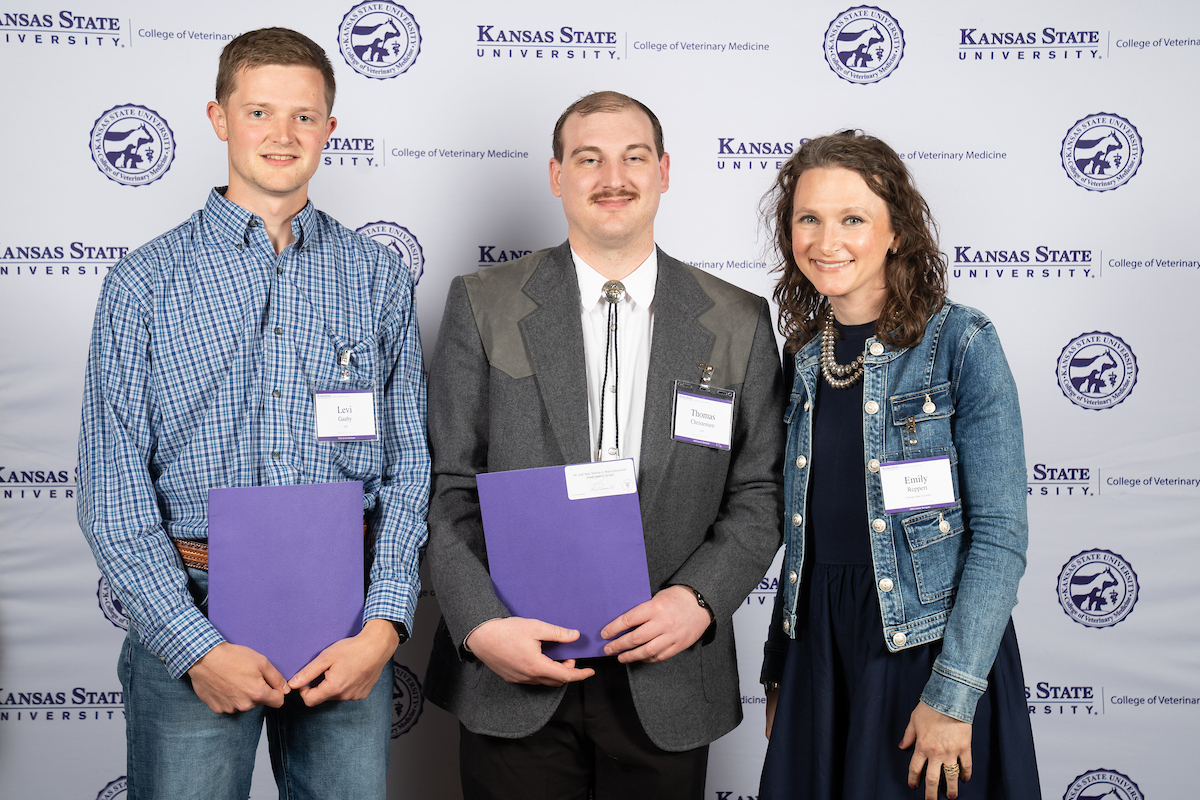 Three people stand in front of a backdrop smiling.