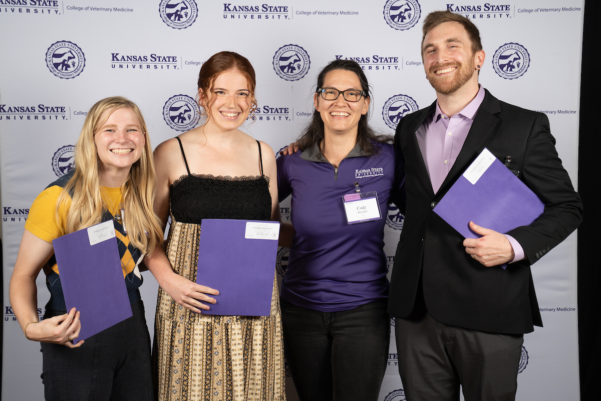 Four people stand in front of a backdrop smiling.