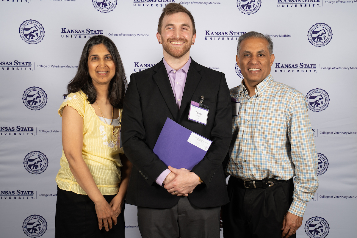 Three people stand in front of a backdrop smiling.