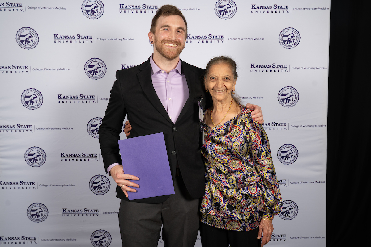 Two people stand in front of a backdrop smiling.