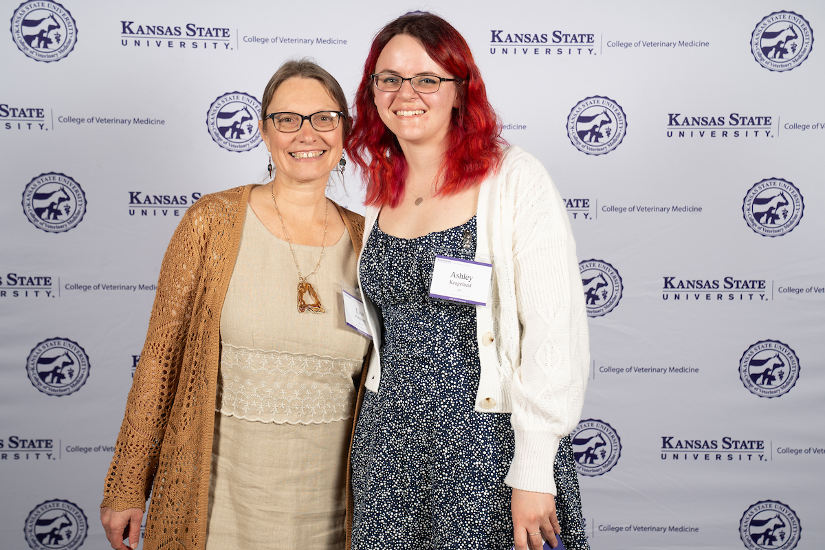 Two people stand in front of a backdrop smiling.