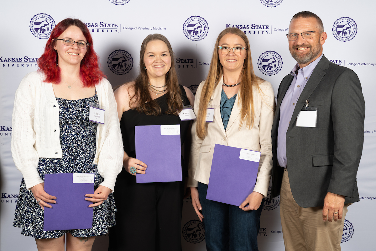 Four people stand in front of a backdrop smiling.