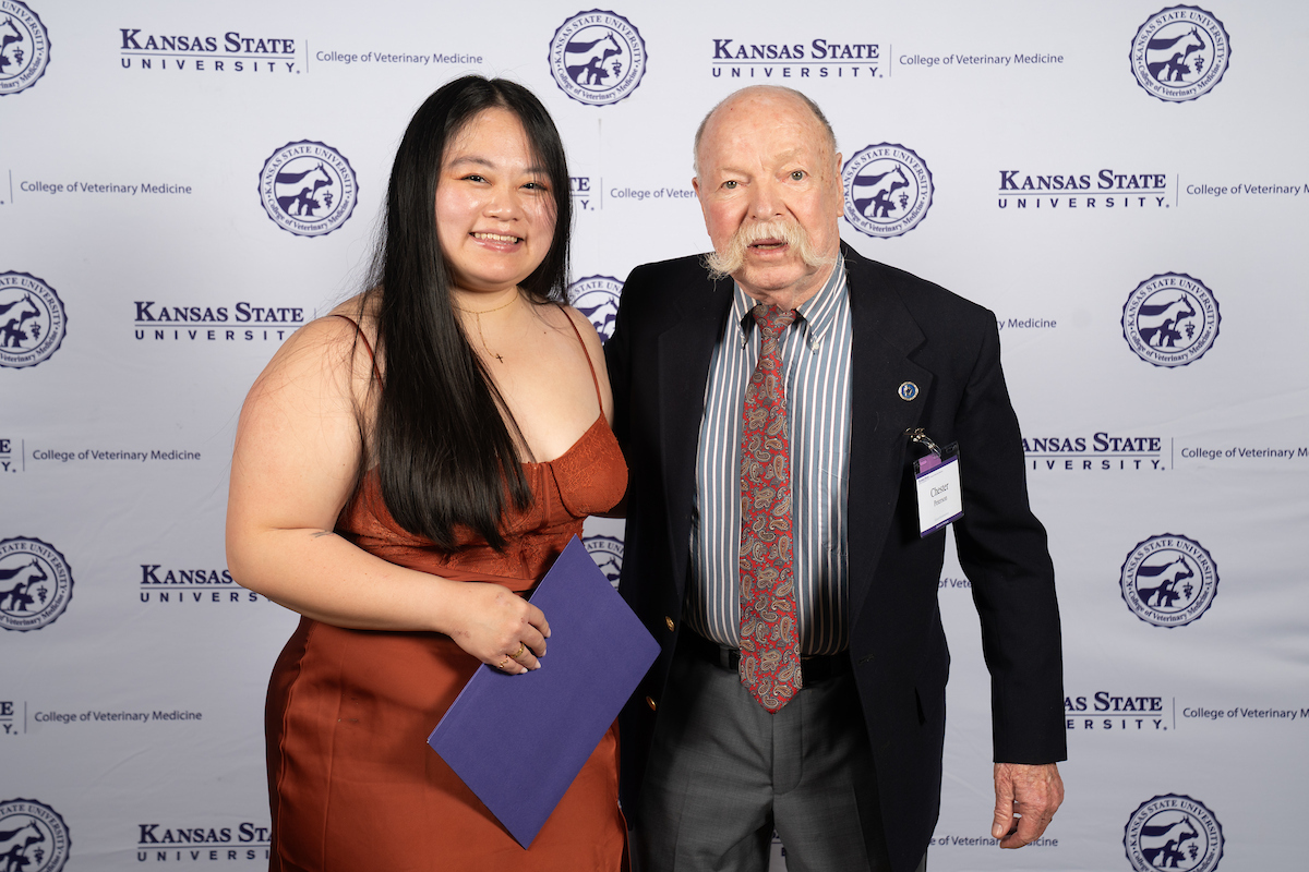 Two people stand in front of a backdrop smiling.