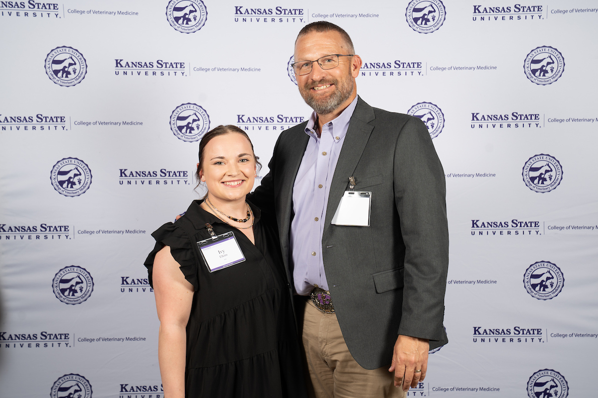 Two people stand in front of a backdrop smiling.