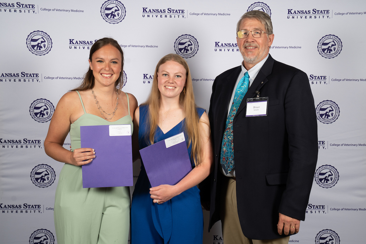 Three people stand in front of a backdrop smiling.