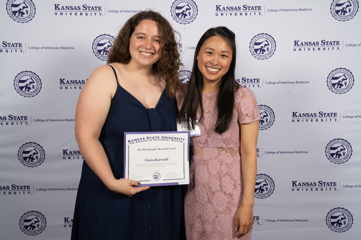Two people stand in front of a backdrop smiling.