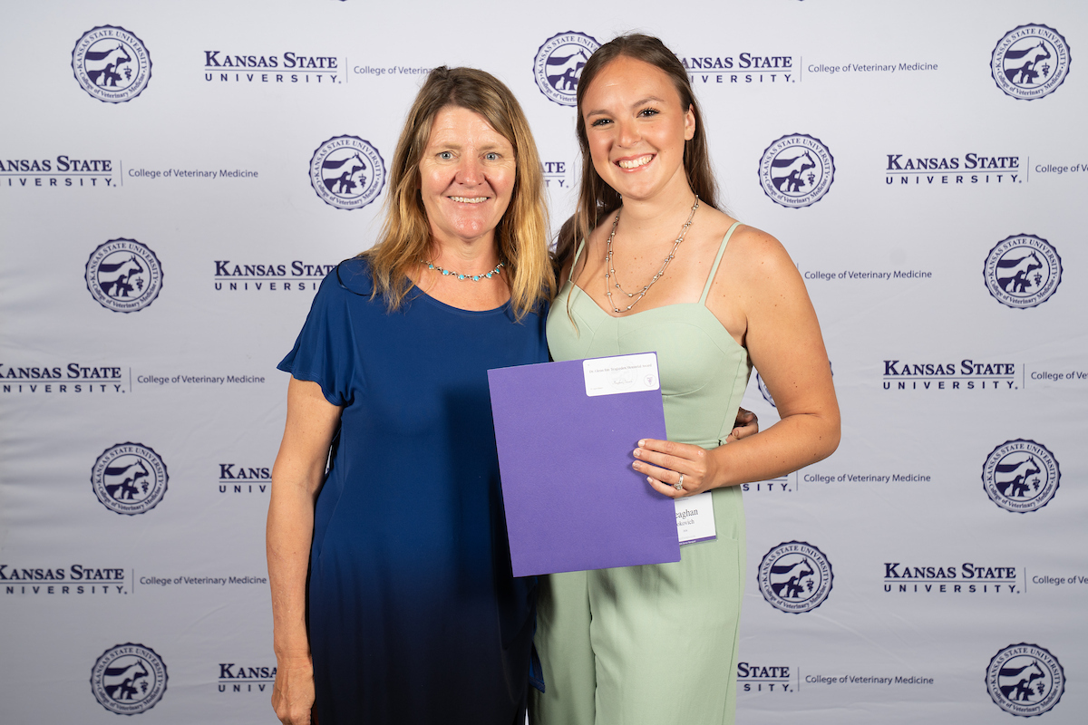 Two people stand in front of a backdrop smiling.