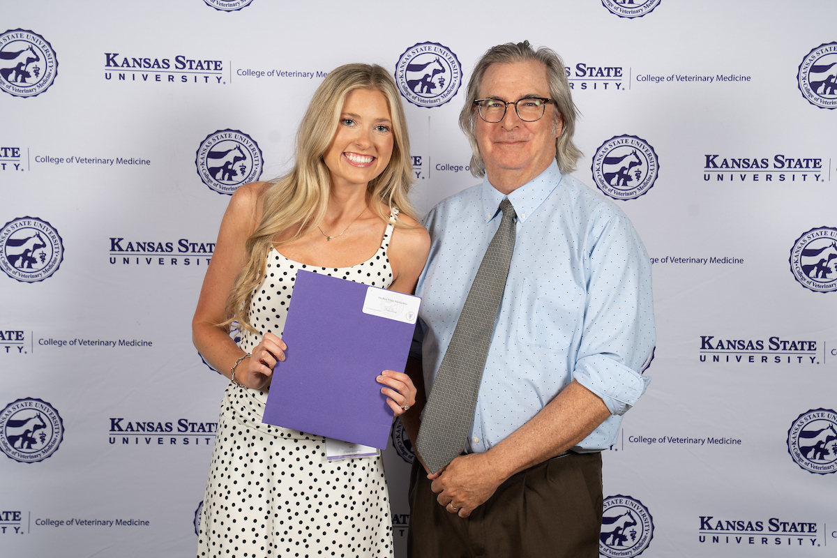 Two people stand in front of a backdrop smiling.