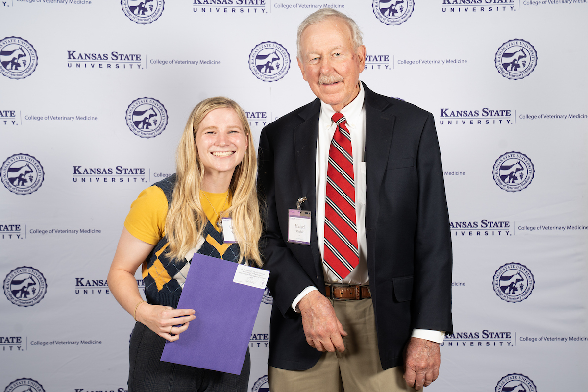 Two people stand in front of a backdrop smiling.