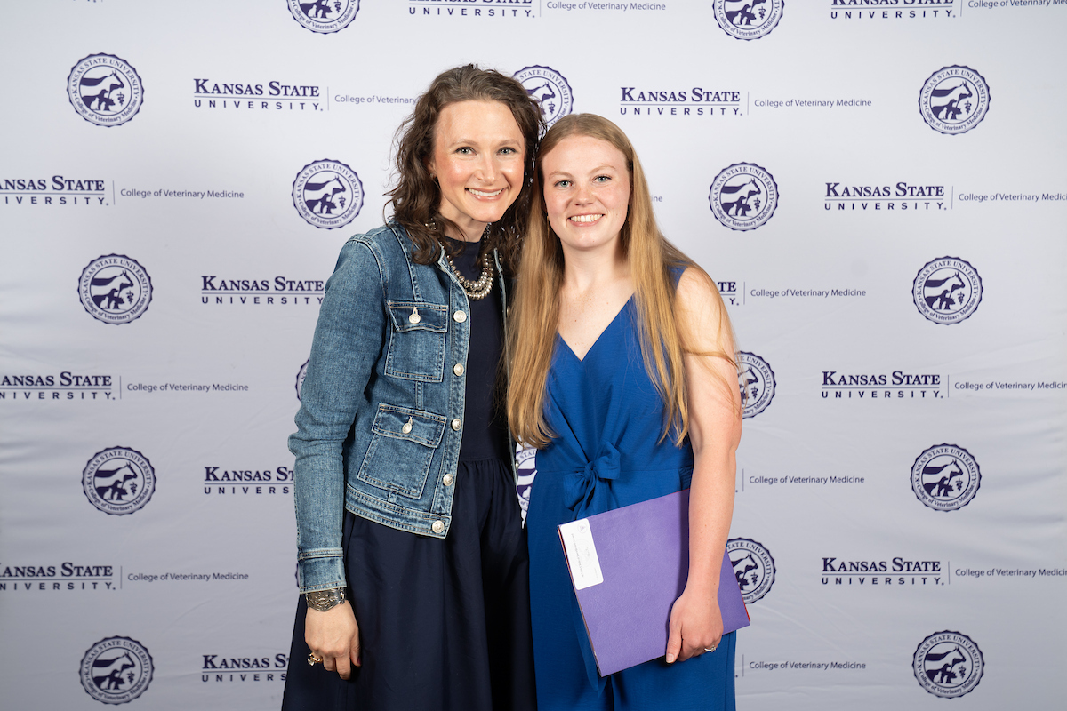 Two women stand in front of a backdrop smiling.