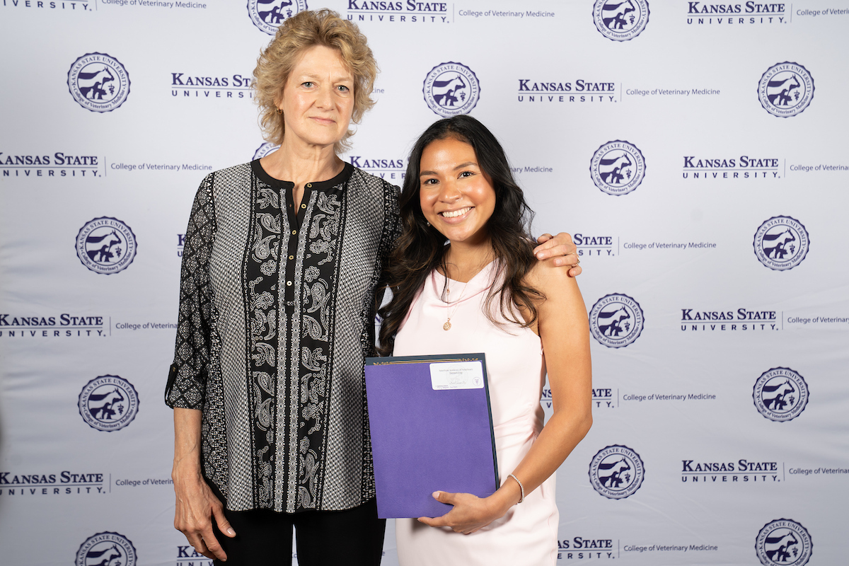 Two people stand in front of a backdrop smiling.