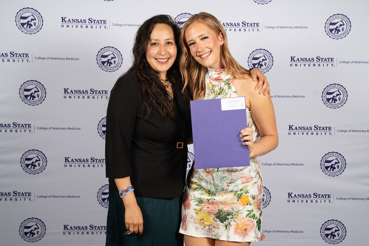 Two people stand in front of a backdrop smiling.