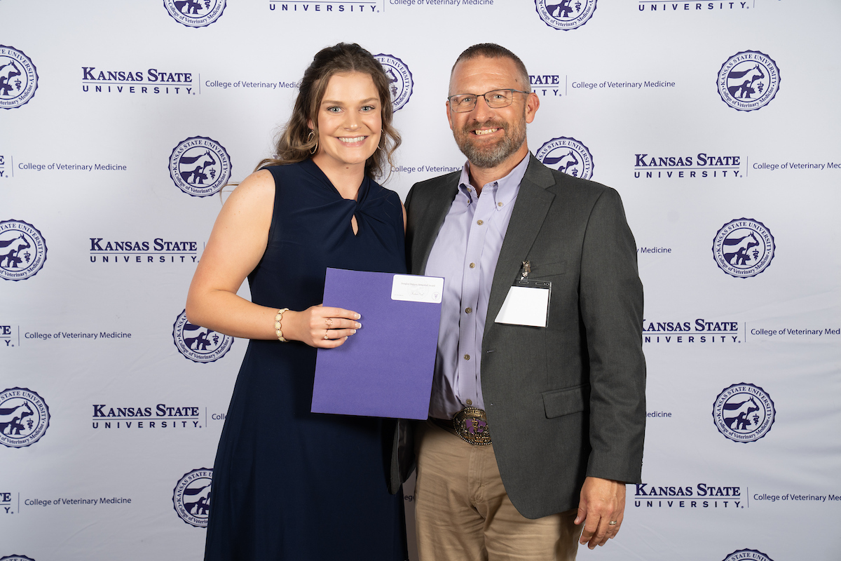 Two people stand in front of a backdrop smiling.
