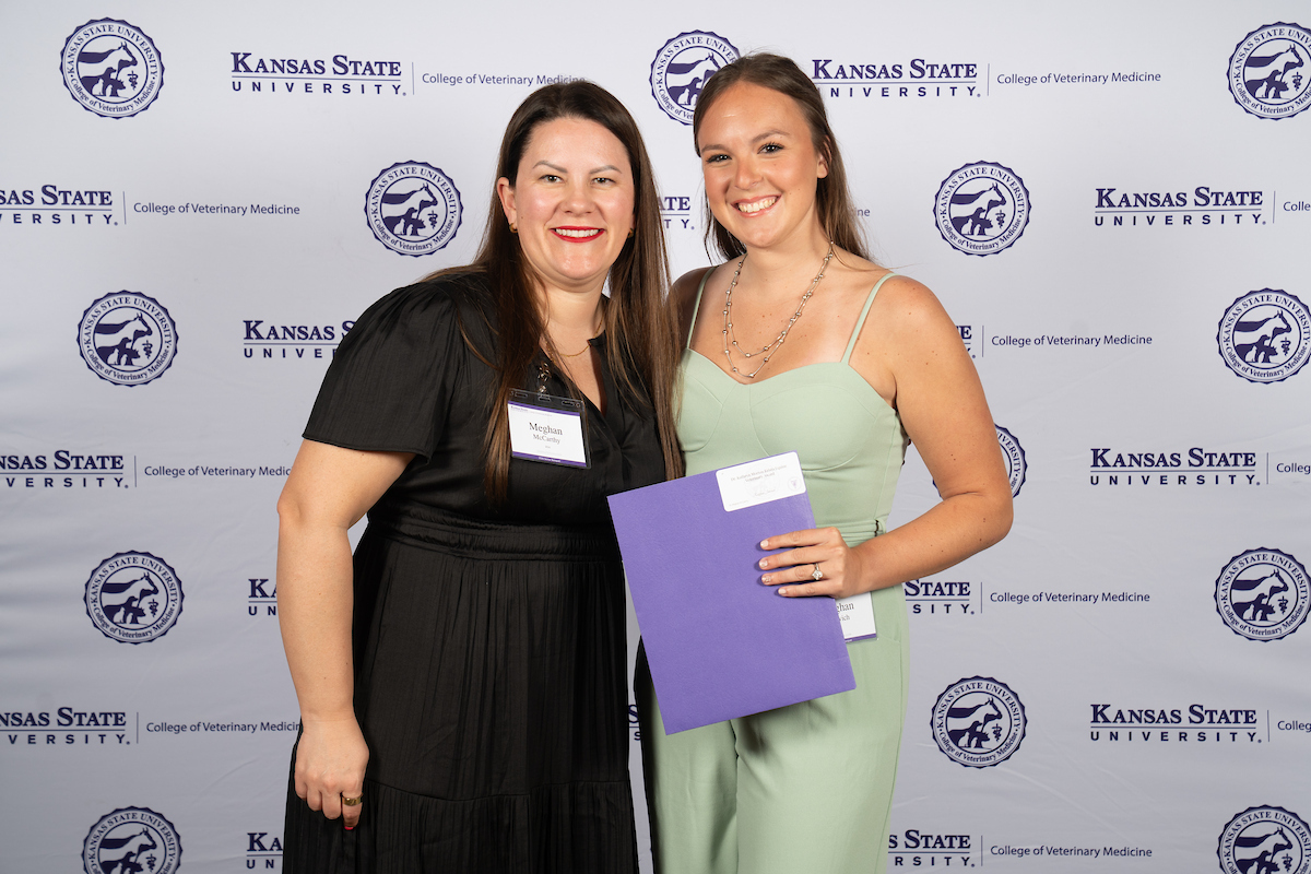 Two people stand in front of a backdrop smiling.
