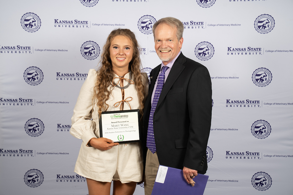 Two people stand in front of a backdrop smiling.