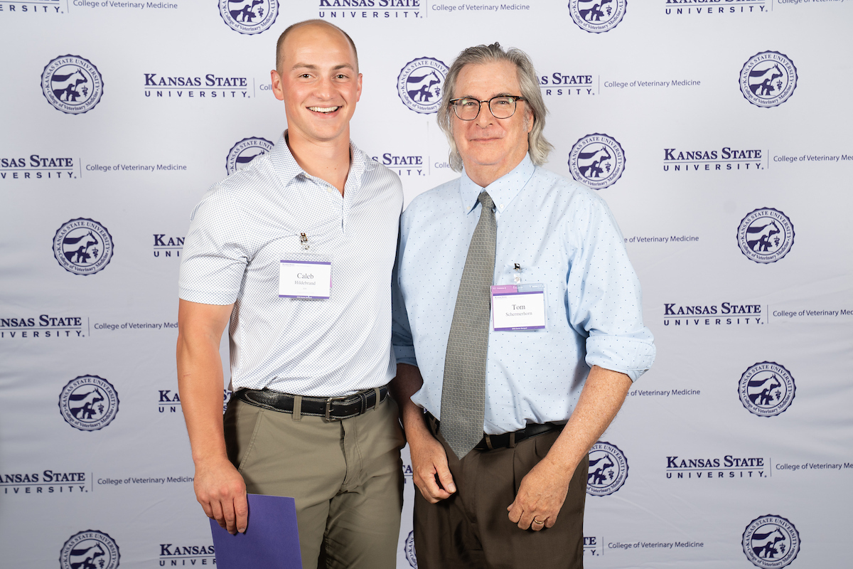Two people stand in front of a backdrop smiling.