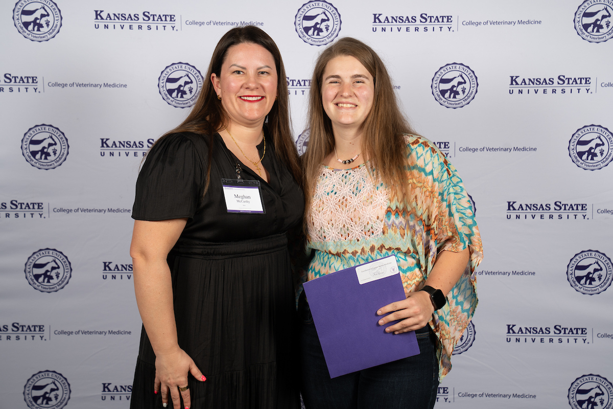Two people stand in front of a backdrop smiling.