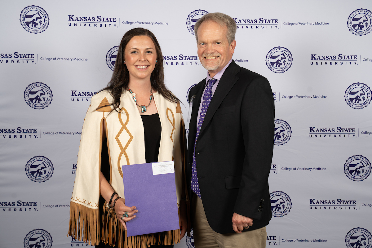 Two people stand in front of a backdrop smiling.