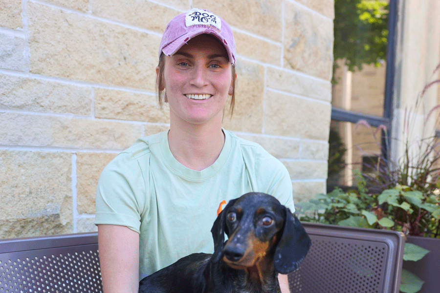 A woman sits on a bench, gently holding a small dog in her lap, enjoying a peaceful moment outdoors.