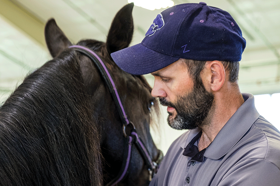 A man in a hat gently pets a horse, showcasing a moment of connection between them.