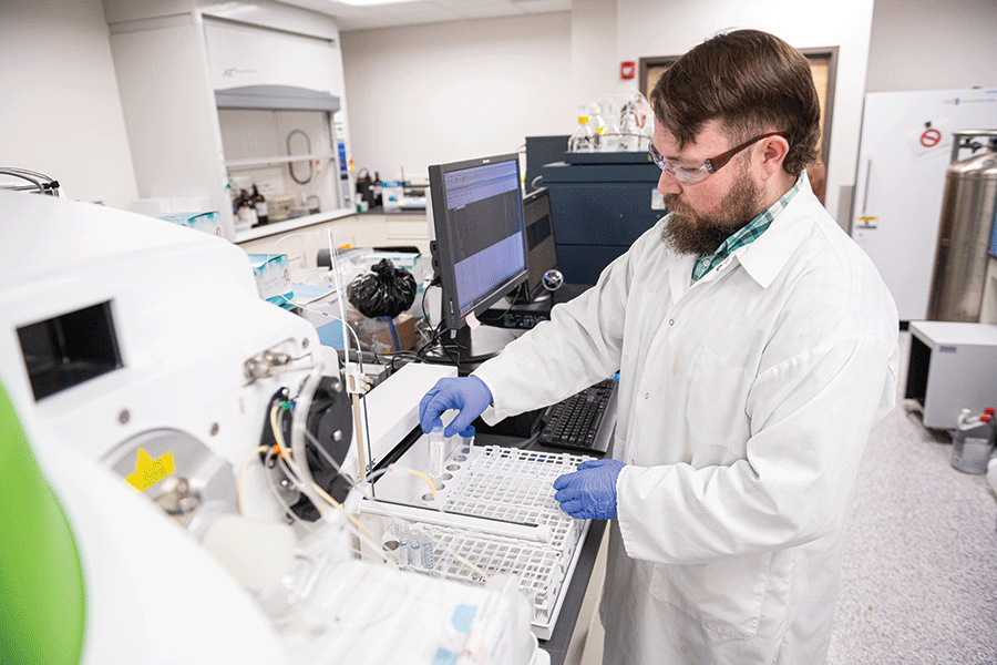 A man wearing a lab coat is engaged in computer work, surrounded by laboratory equipment.