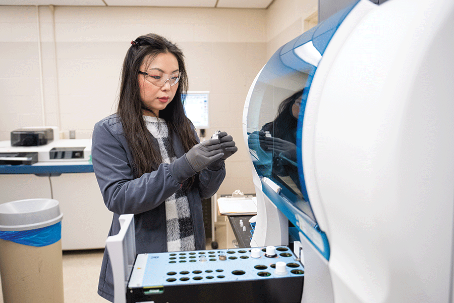A woman in a lab coat examines a machine, focused on its operation and functionality in a laboratory setting.