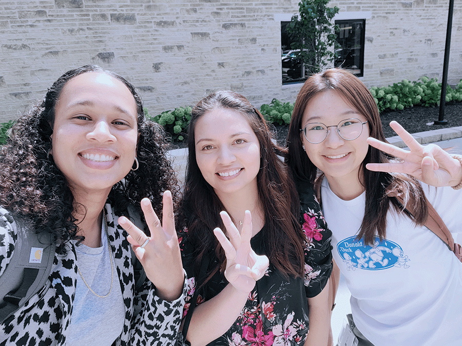 Three women stand together, smiling and raising their hands in a joyful pose for the camera.