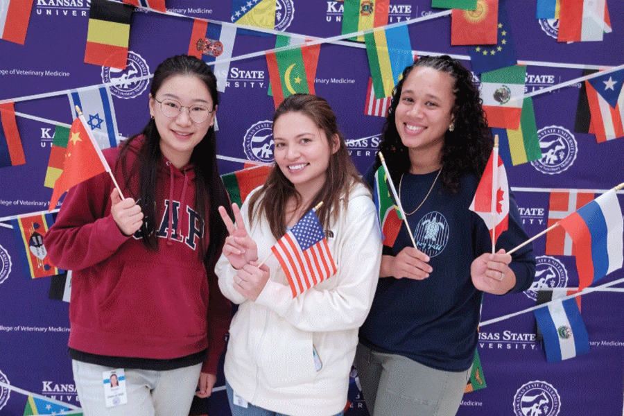 Three girls display flags in front of a vibrant banner, symbolizing teamwork and celebration.